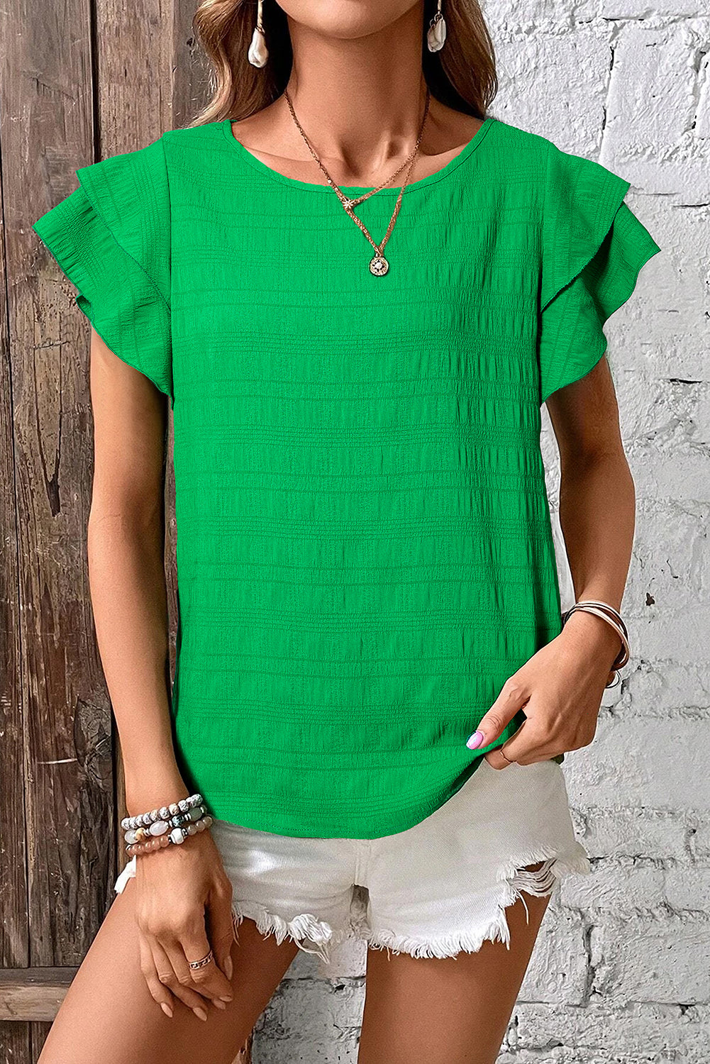 Person wearing a green top with ruffled sleeves against a white brick wall.