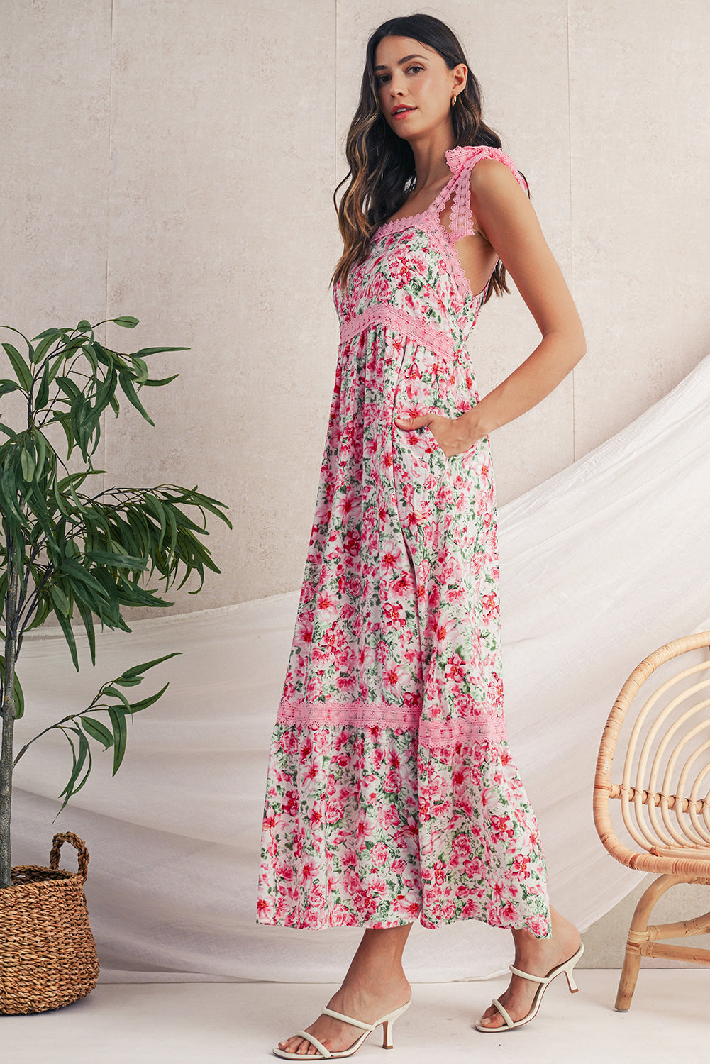 Woman wearing a floral dress standing in a room with a plant and chair.