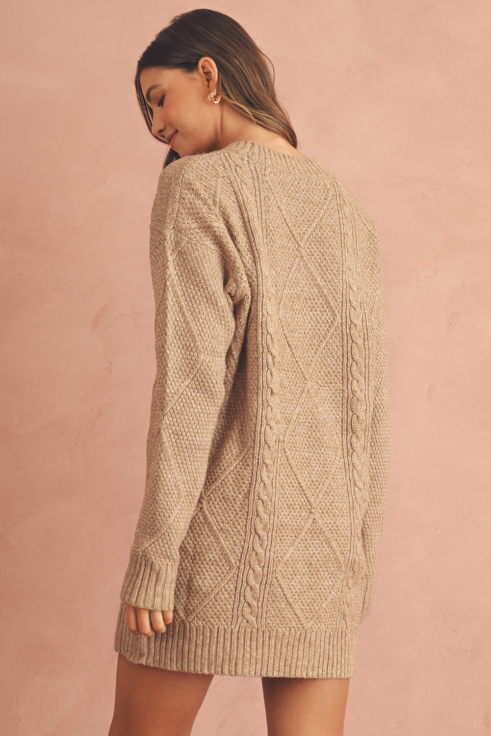 Woman wearing a beige cable knit sweater against a pink background