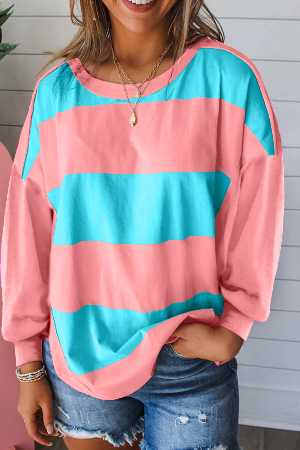 Person wearing a pink and blue striped sweater with denim shorts against a light wooden panel background.