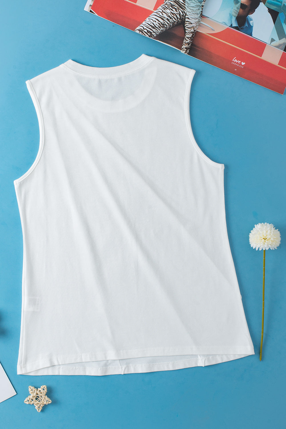 White sleeveless top on a blue background with a dandelion and decorative item.