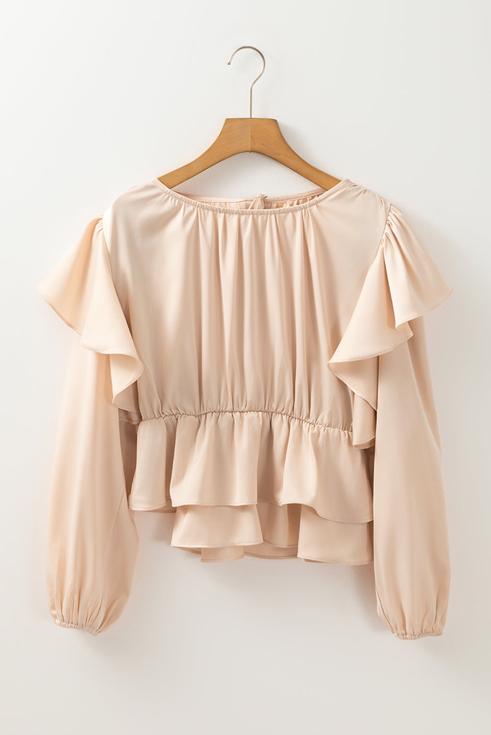 Beige blouse with ruffled layers on a wooden hanger against a white background