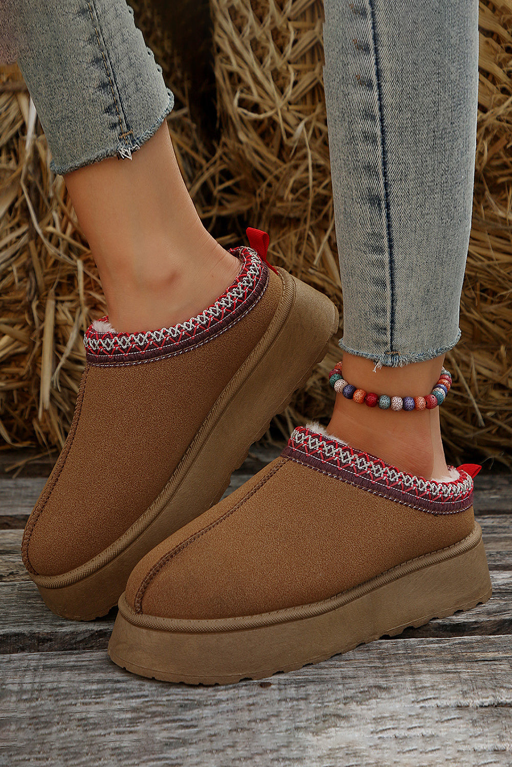 Brown slip-on shoes with decorative straps worn by a person on a wooden floor.