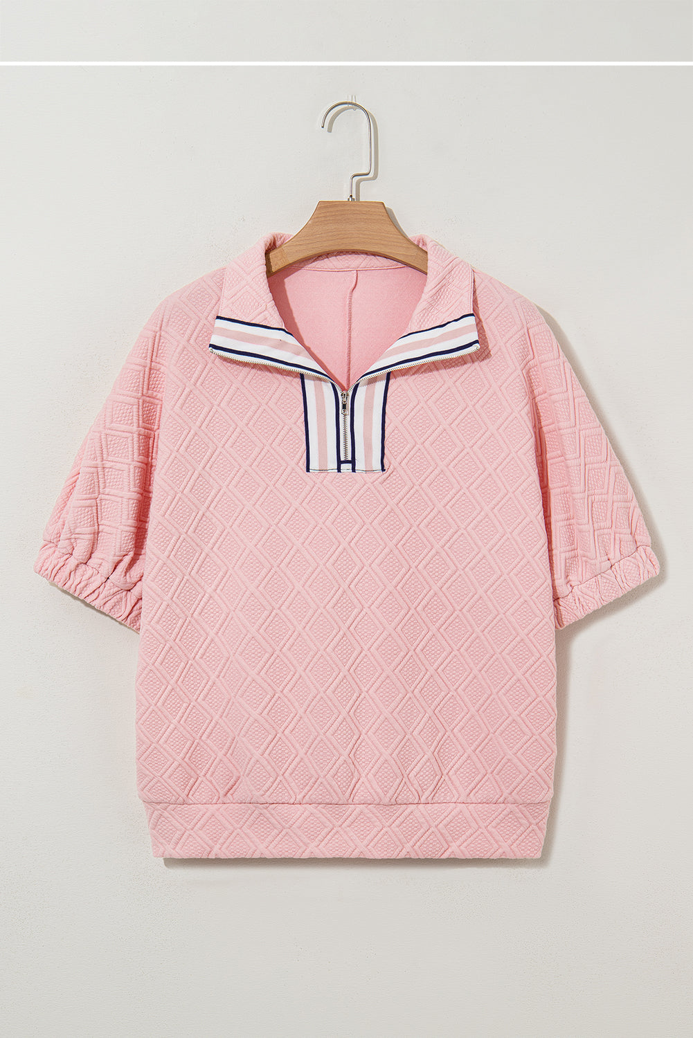 Pink quilted jacket with a striped collar on a hanger against a light gray background