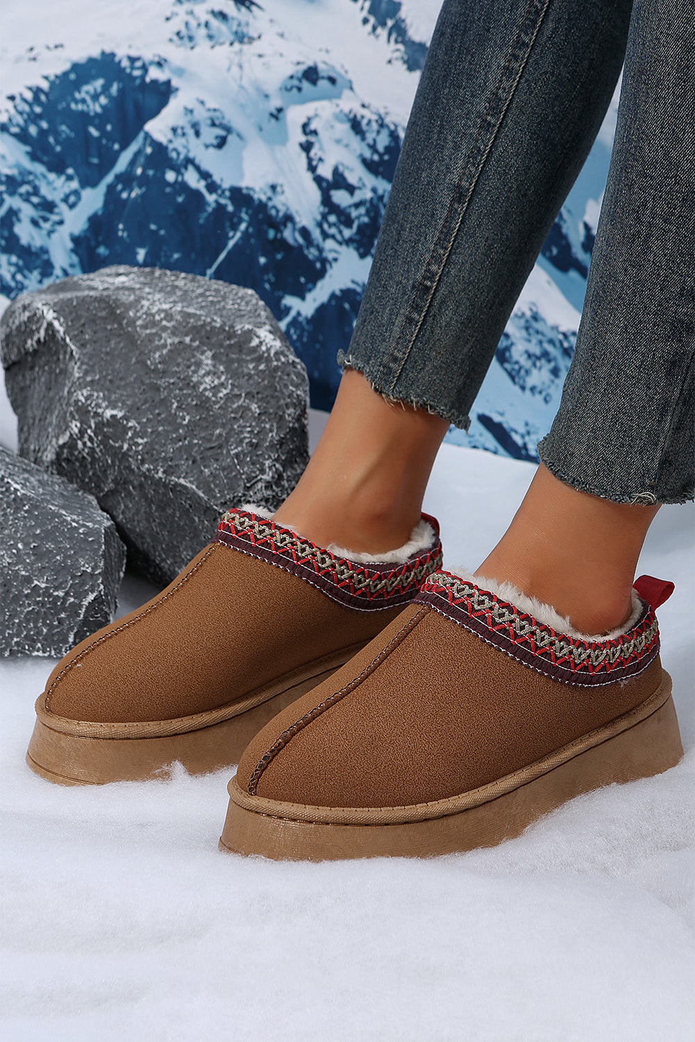 Brown slip-on shoes with red accents worn in a snowy landscape.