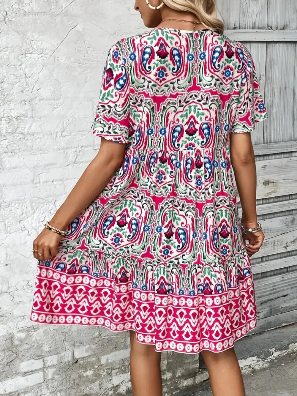 Woman wearing a colorful patterned dress against a textured wall.