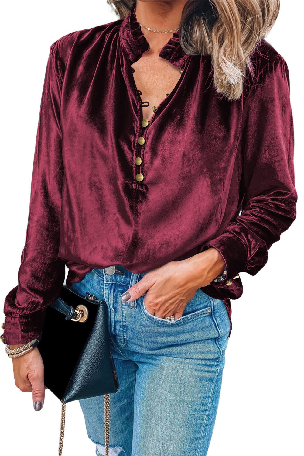 Woman wearing a burgundy velvet shirt and blue jeans, holding a black handbag.