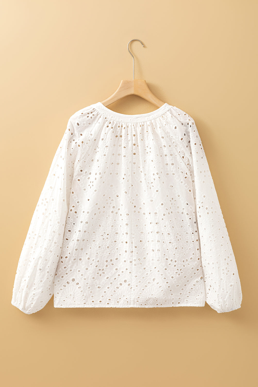 White blouse with long sleeves on a wooden hanger against a beige background