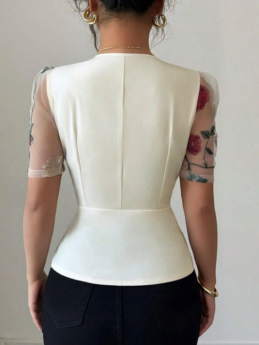 Person wearing a white top with sheer sleeves against a plain background