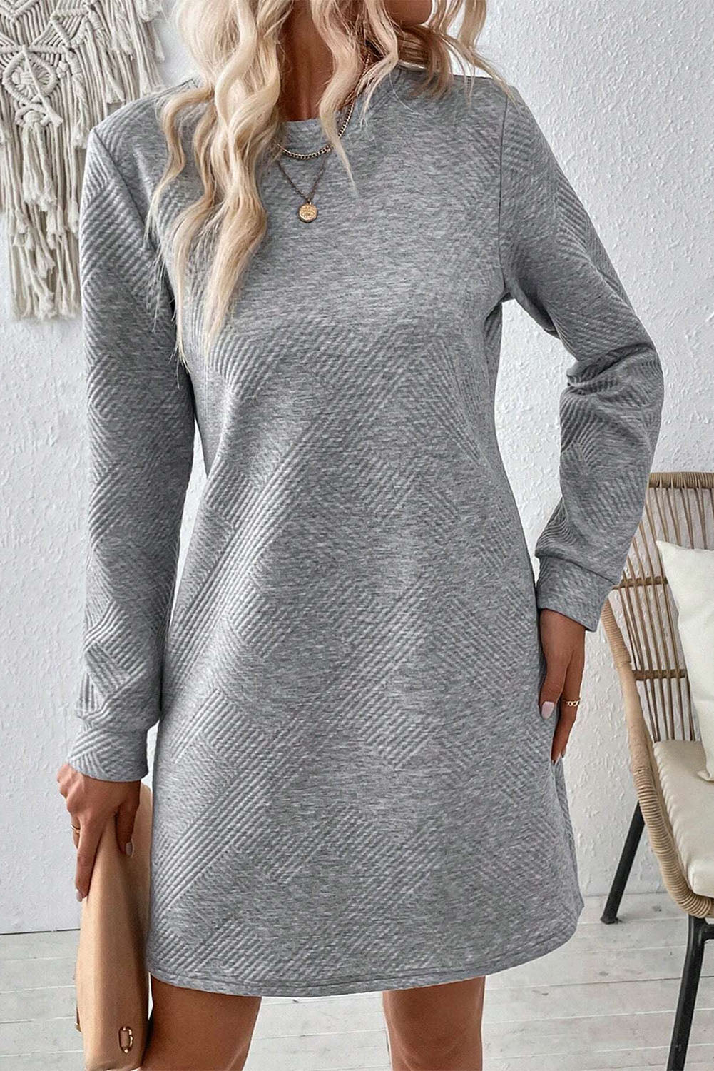 Woman wearing a gray long-sleeve dress in a room with a chair and white wall.