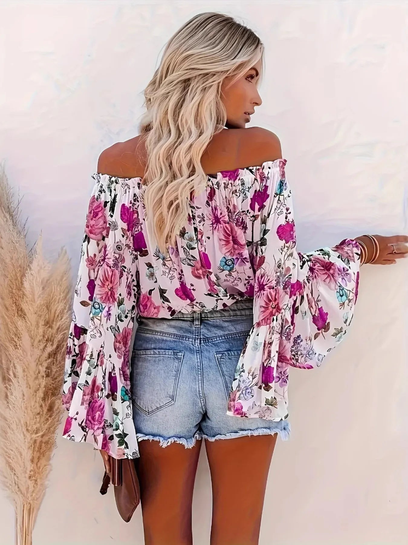Woman wearing a floral off-shoulder top and denim shorts against a white background