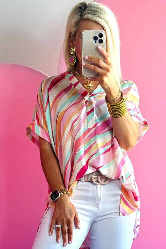 Person wearing a colorful striped shirt and white pants against a pink background
