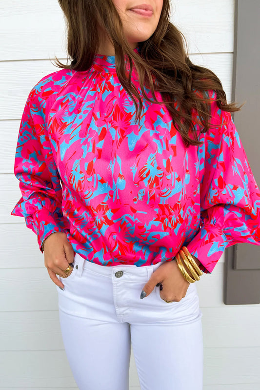 Person wearing a bright pink and blue patterned blouse with white pants against a light background