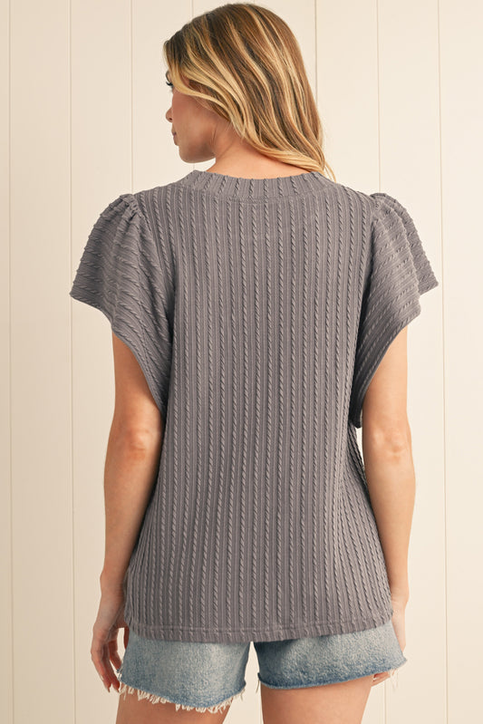 Woman wearing a gray ribbed sweater and denim shorts against a beige wall.