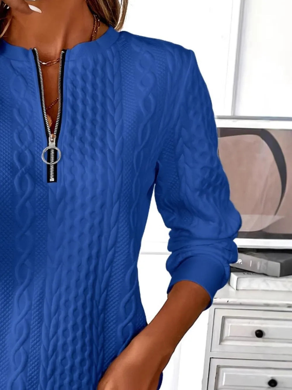 Blue cable knit sweater with a zipper worn by a person, indoors.