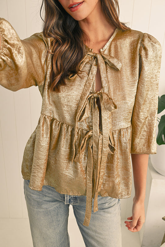 Woman wearing a gold metallic blouse with puffed sleeves and tied front, paired with light blue jeans.