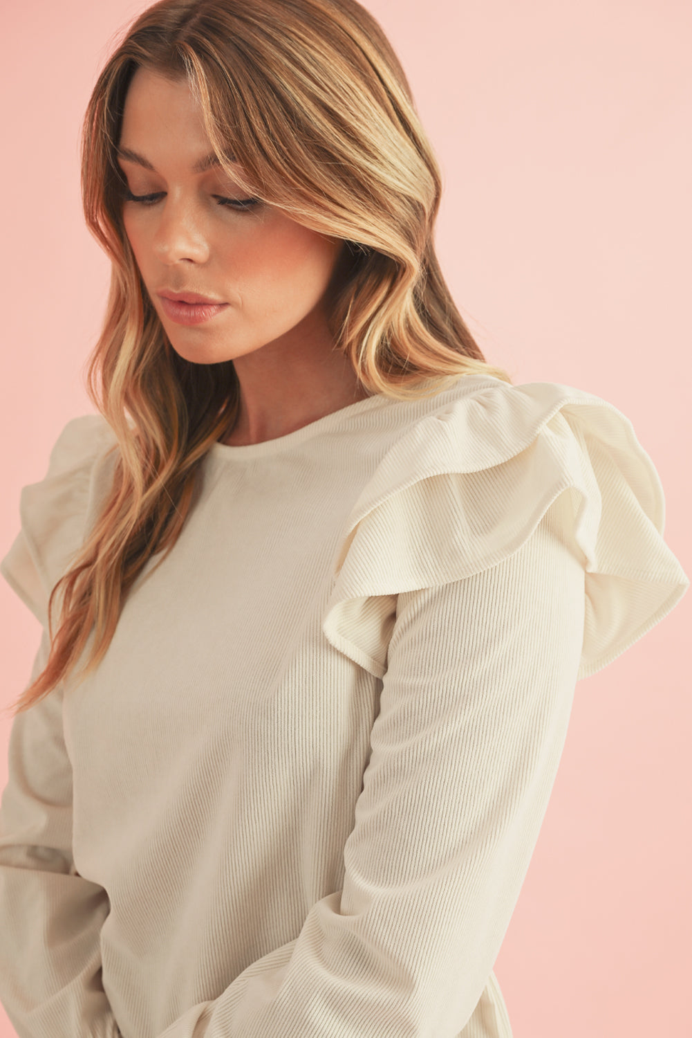 Woman wearing a beige blouse with ruffled sleeves against a pink background