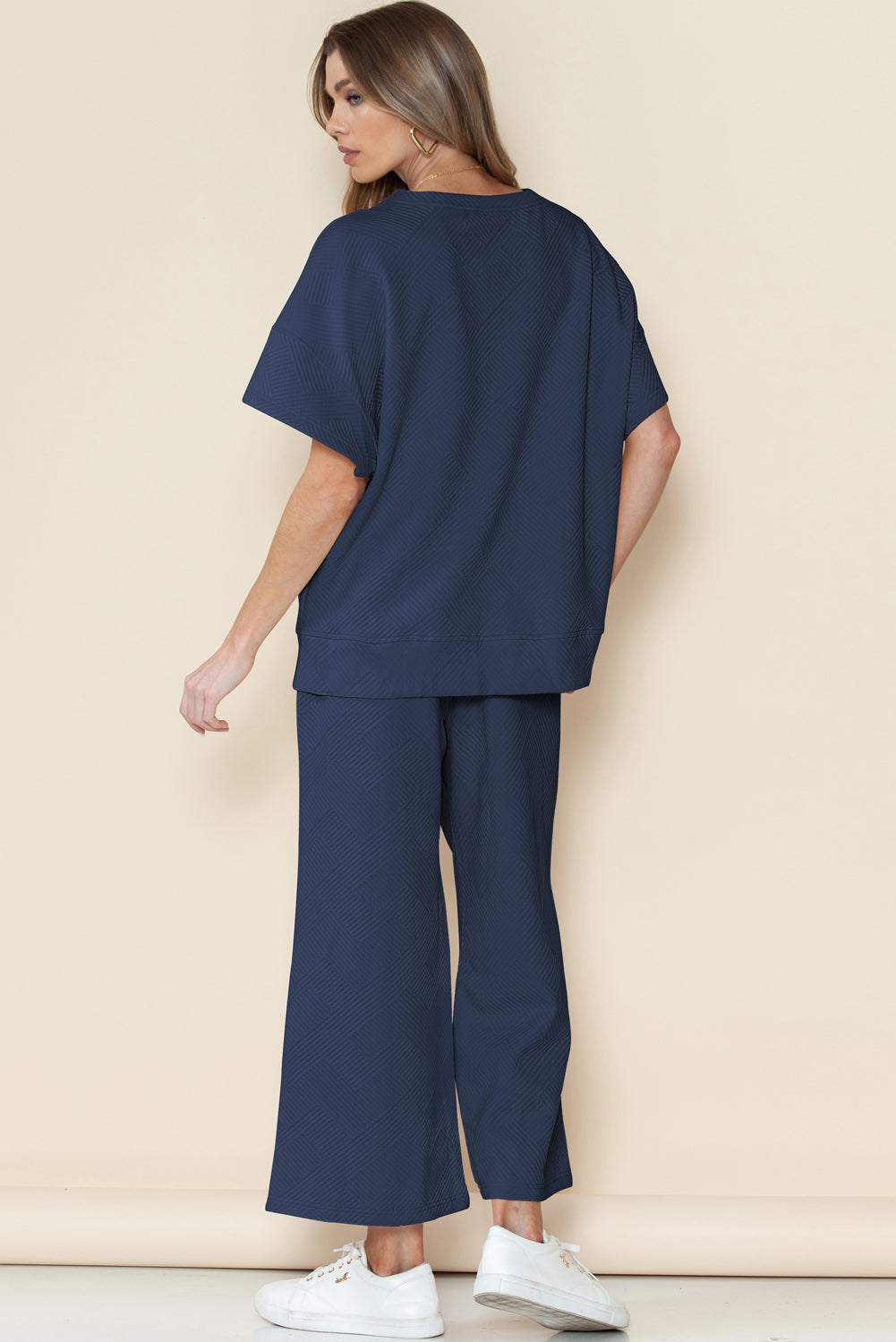 Woman wearing a navy blue outfit with wide-leg pants against a beige background