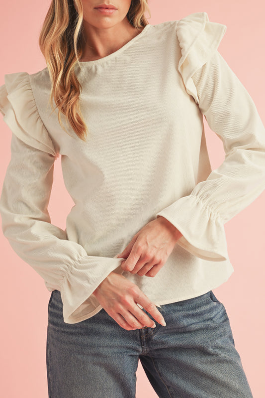 Woman wearing a cream blouse with ruffled sleeves against a pink background