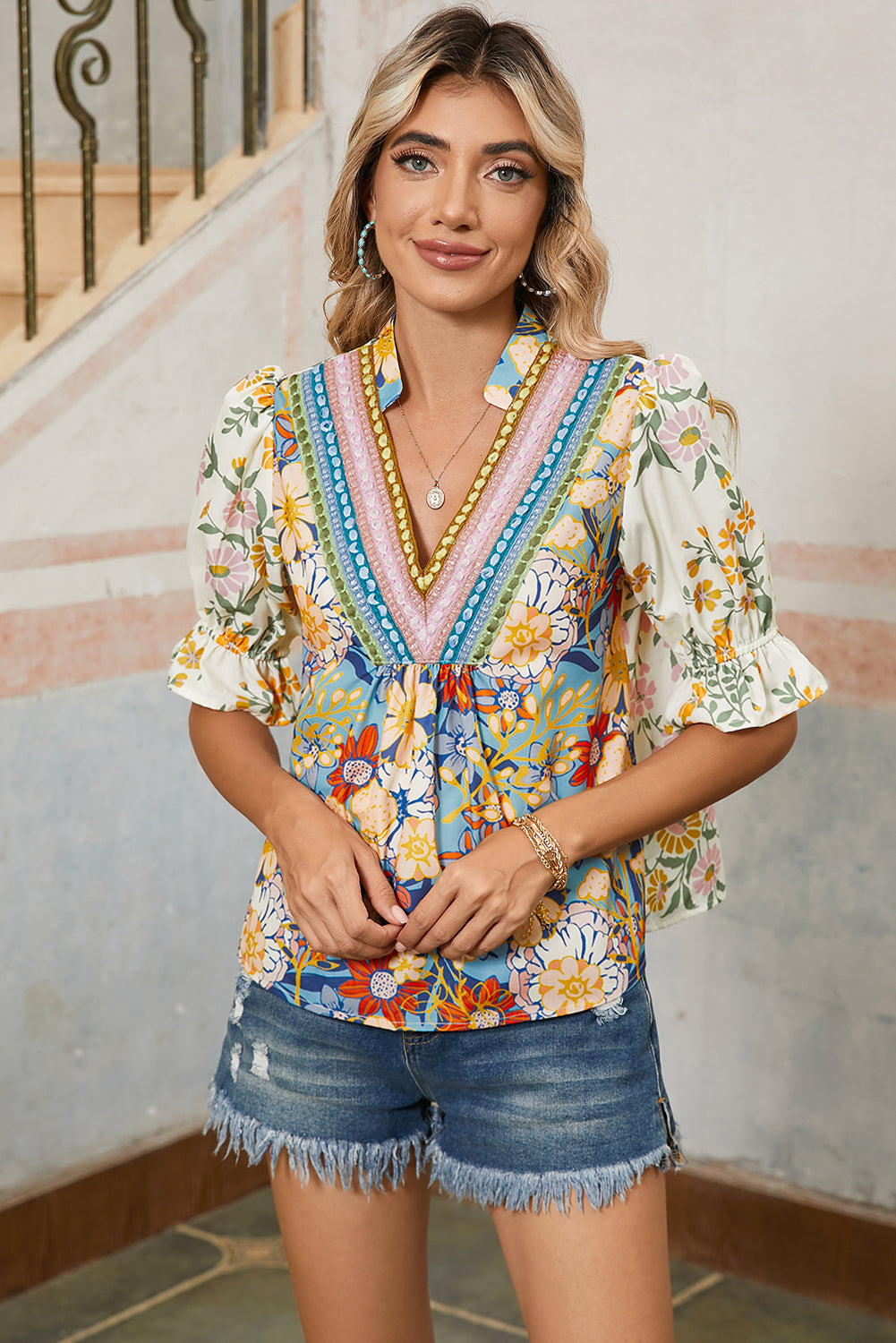 Woman wearing a colorful floral blouse and denim shorts indoors.