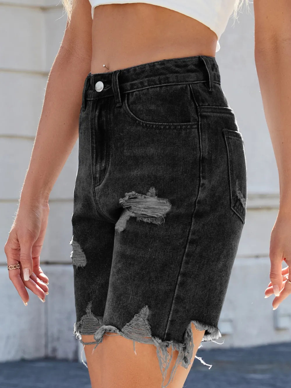 Black denim shorts with distressed details worn by a person, against a neutral background.