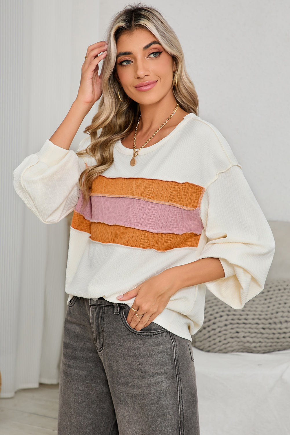 Woman wearing a white blouse with colorful stripes and gray pants against a neutral background