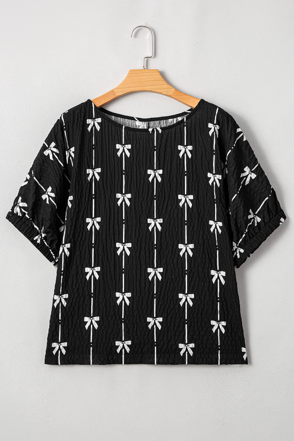 Black blouse with white bow pattern on a wooden hanger against a white background