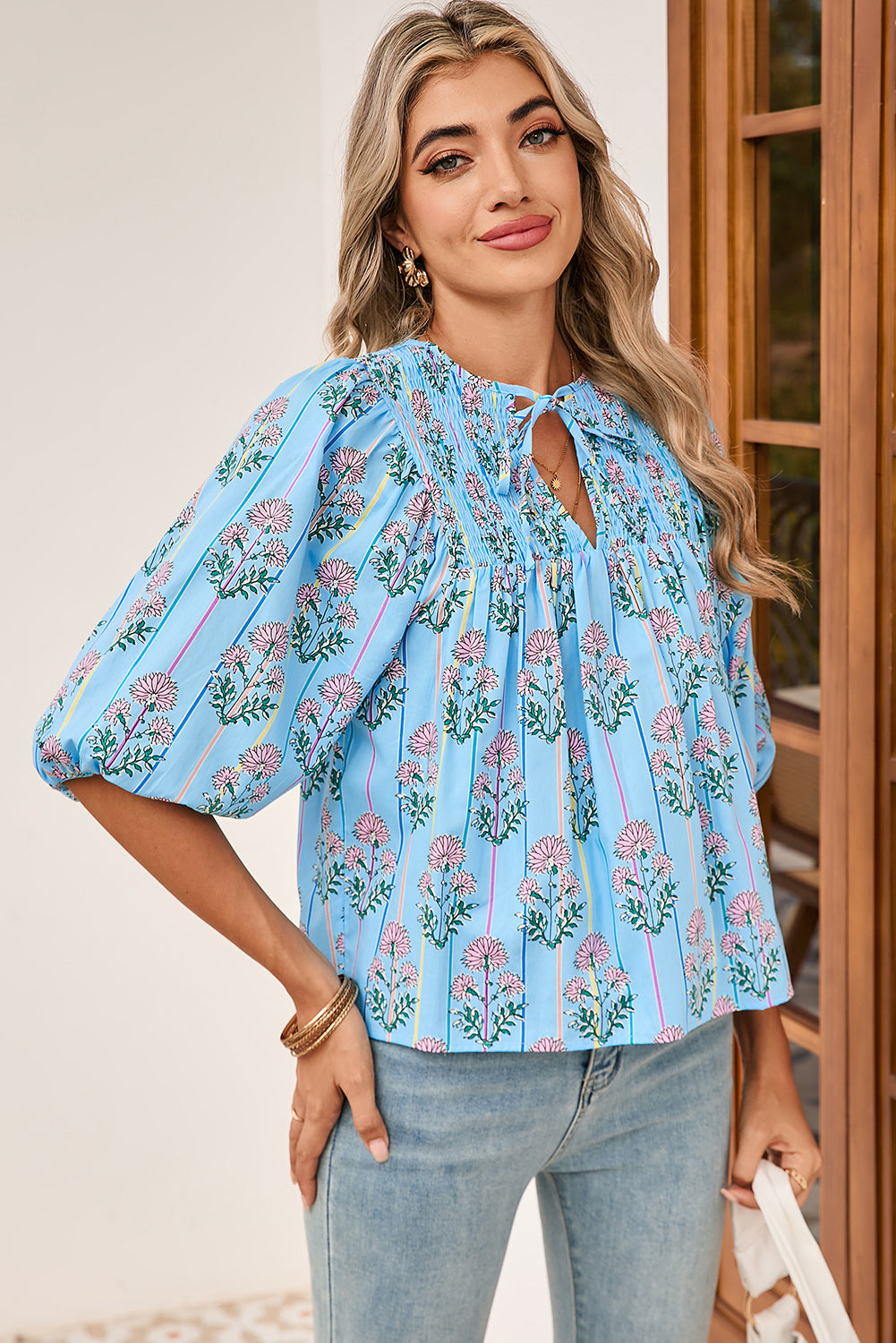 Woman wearing a light blue floral blouse with puffed sleeves indoors.