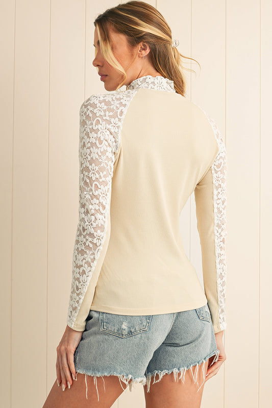 Woman wearing a cream long-sleeve top with lace sleeves against a beige wall.