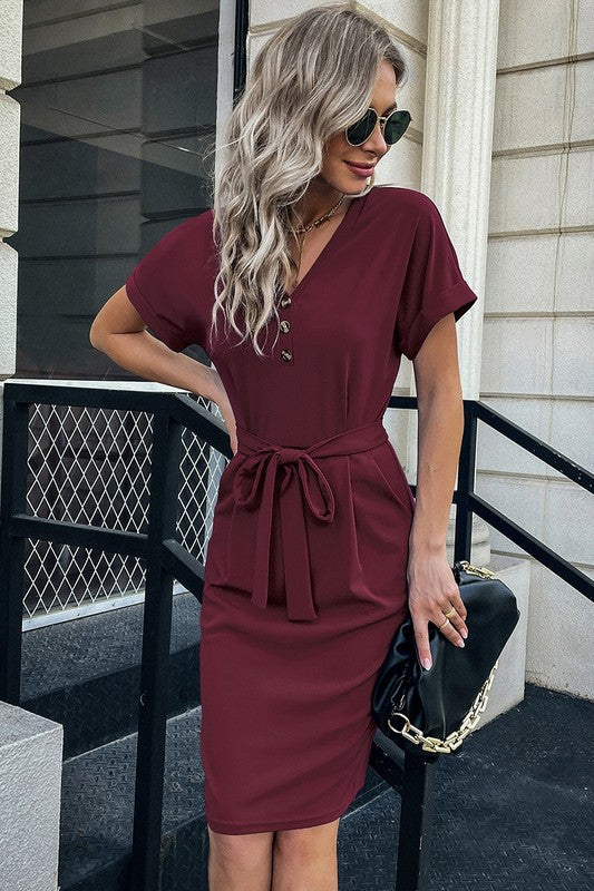 Woman wearing a burgundy dress with a black handbag on a city street.
