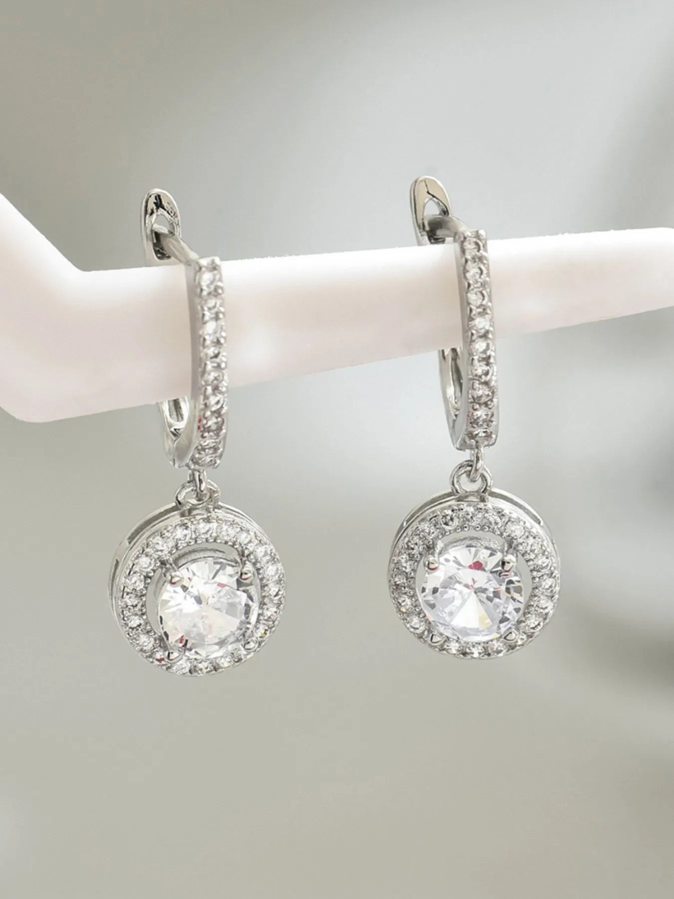 Silver hoop earrings with clear gemstones on a white mannequin arm against a light gray background