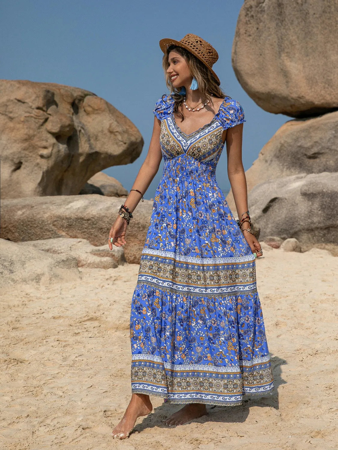 Woman in a blue patterned dress standing on rocky terrain with large stones in the background