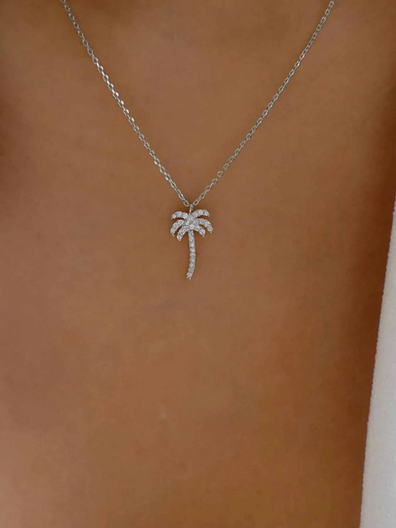 Silver palm tree necklace on a brown background