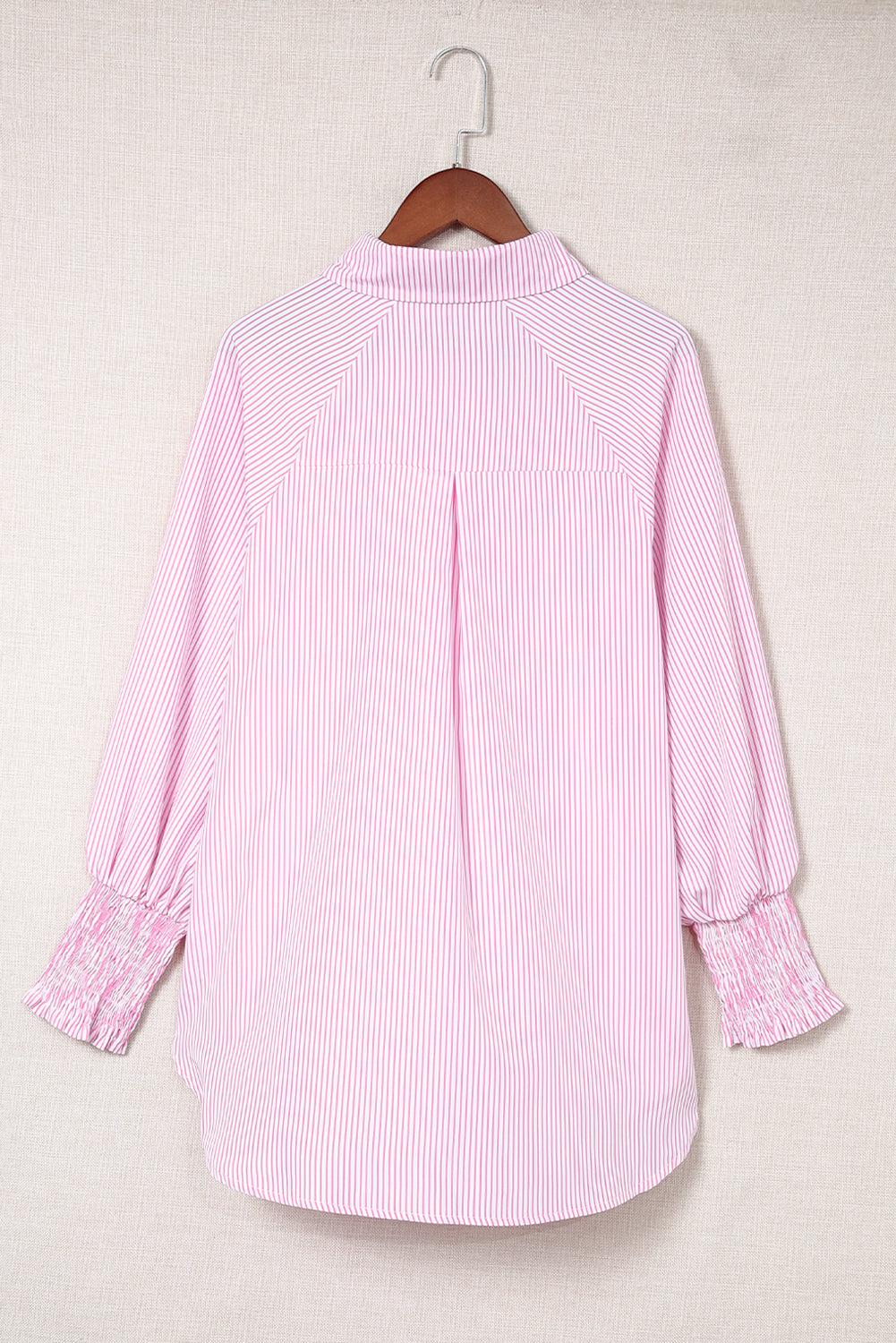 Pink striped shirt on a hanger against a beige background
