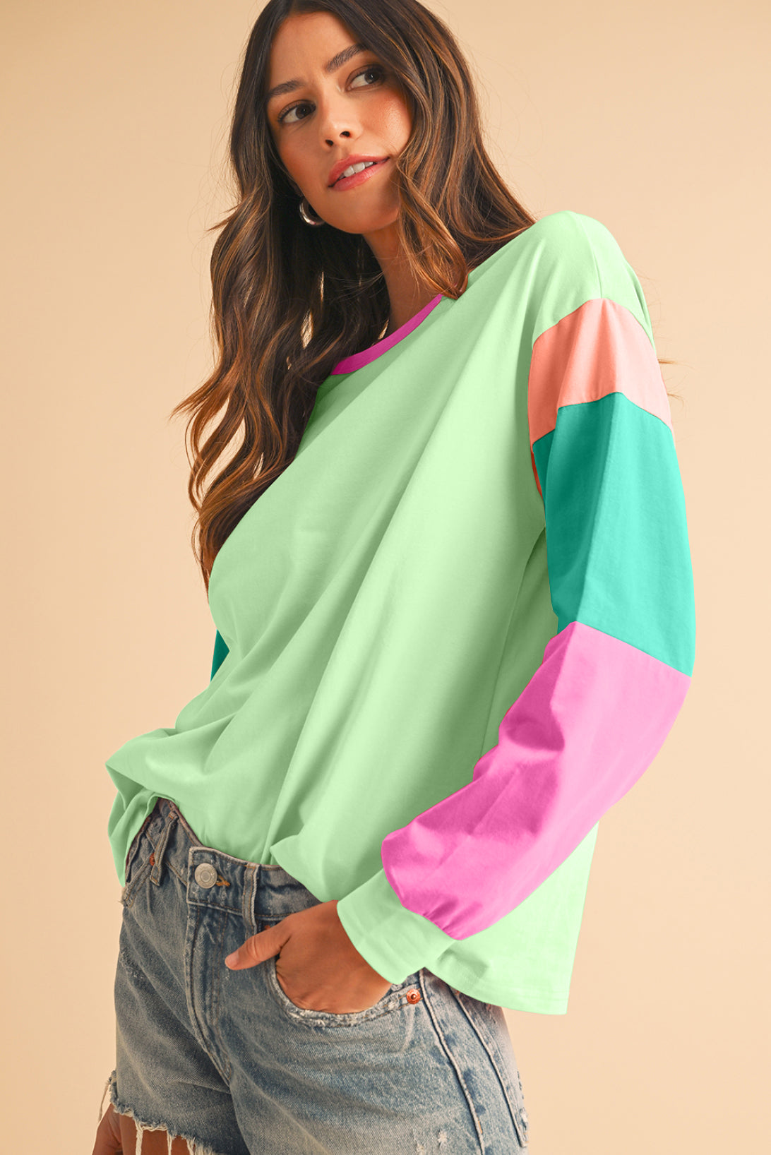 Woman wearing a colorful sweater with green, pink, and blue sleeves on a beige background