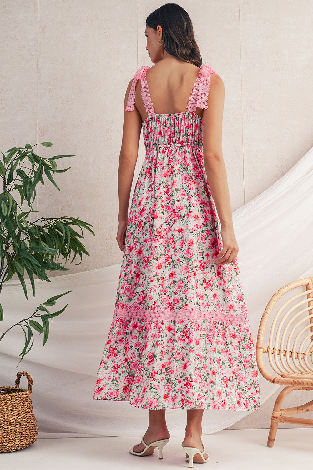 Woman wearing a floral dress standing in a room with a plant and chair.