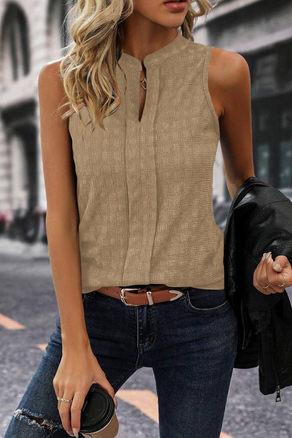 Woman wearing a beige sleeveless top and dark jeans on a city street.