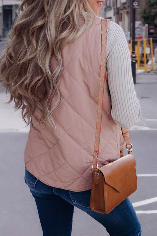 Woman wearing a pink quilted vest and carrying a brown leather bag on a city street.