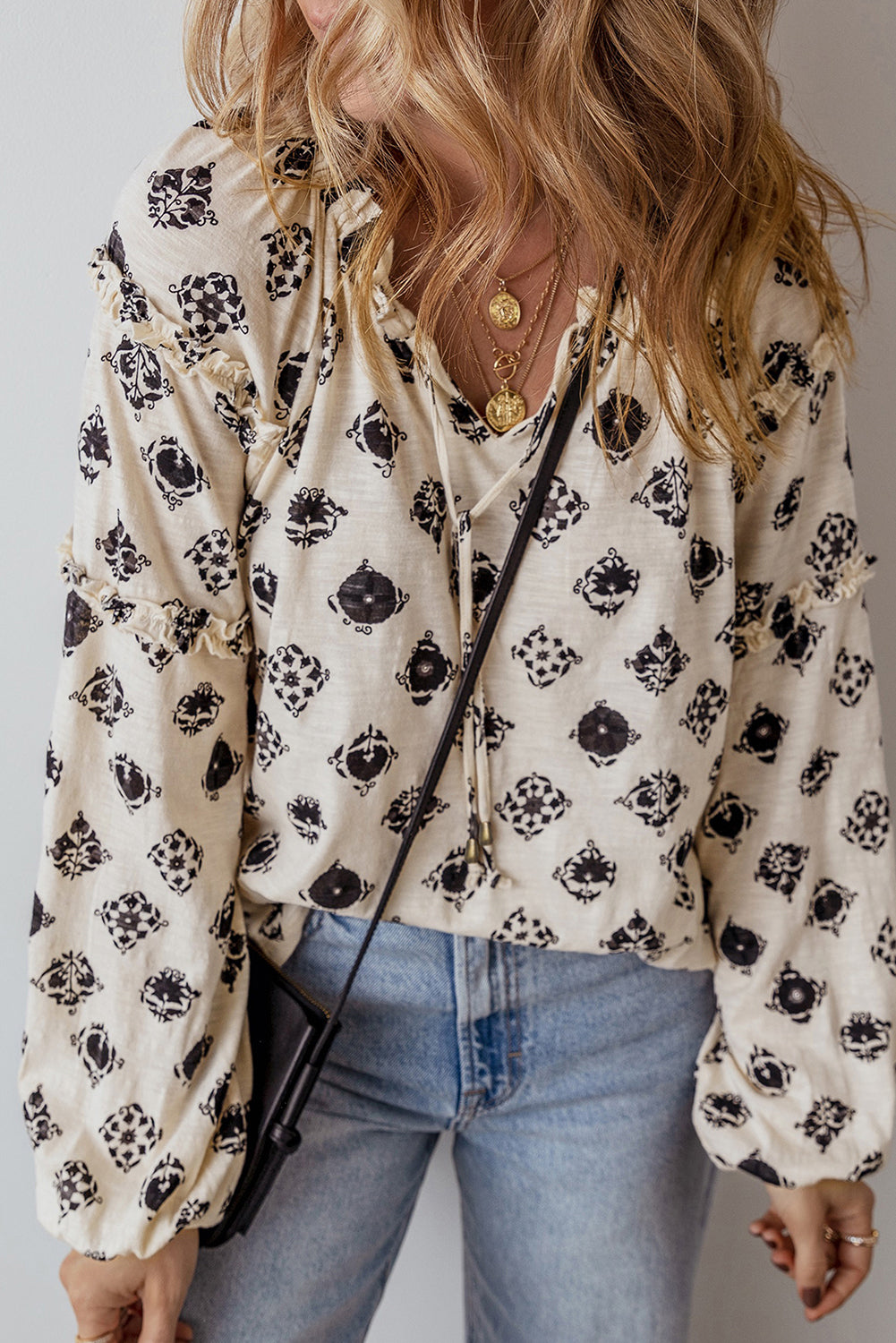 Person wearing a floral blouse with long sleeves and blue jeans against a neutral background