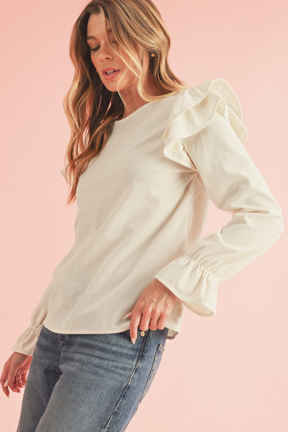 Woman wearing a white blouse with ruffled sleeves against a pink background