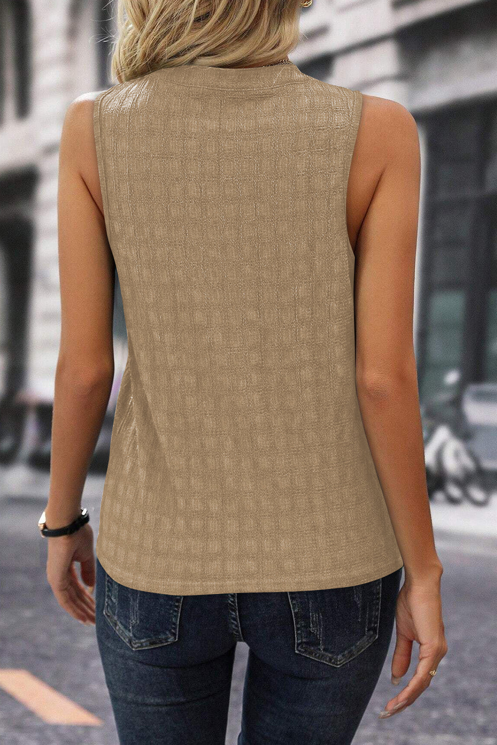 Person wearing a beige sleeveless top and blue jeans on a blurred street background