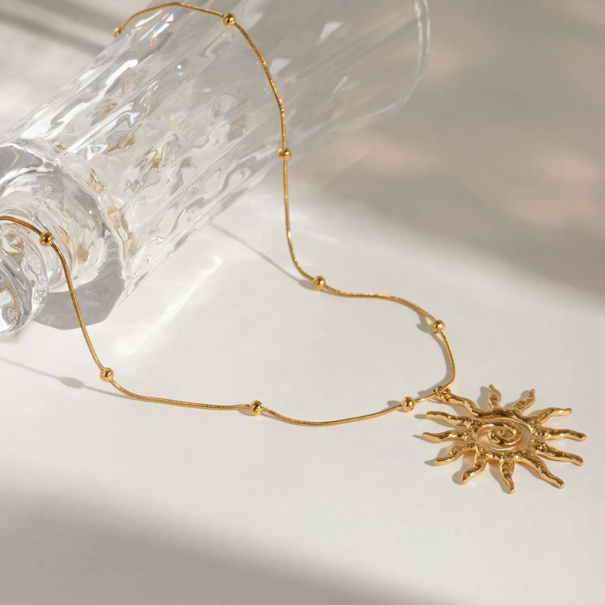Gold necklace with a sun pendant on a light background