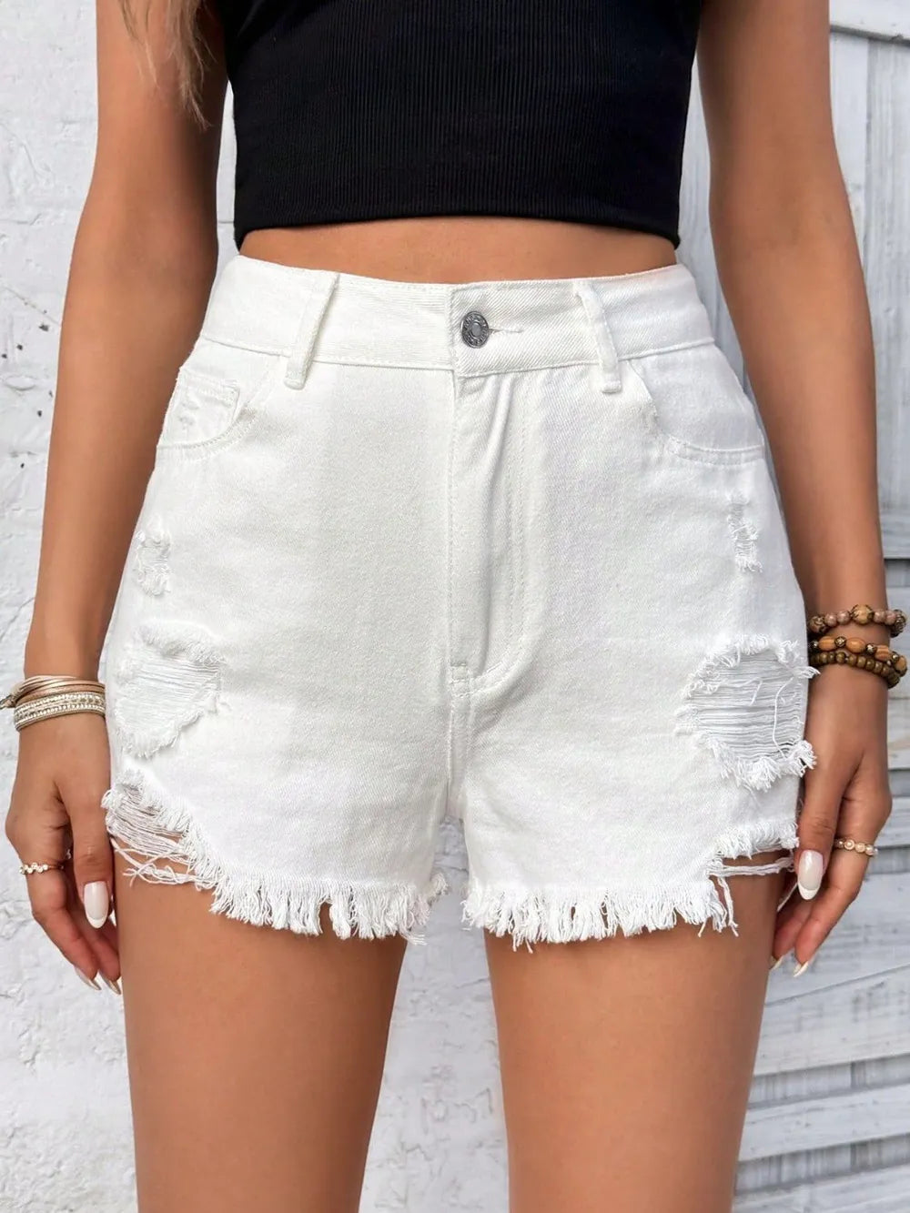 White denim shorts with frayed edges worn by a person against a light gray background