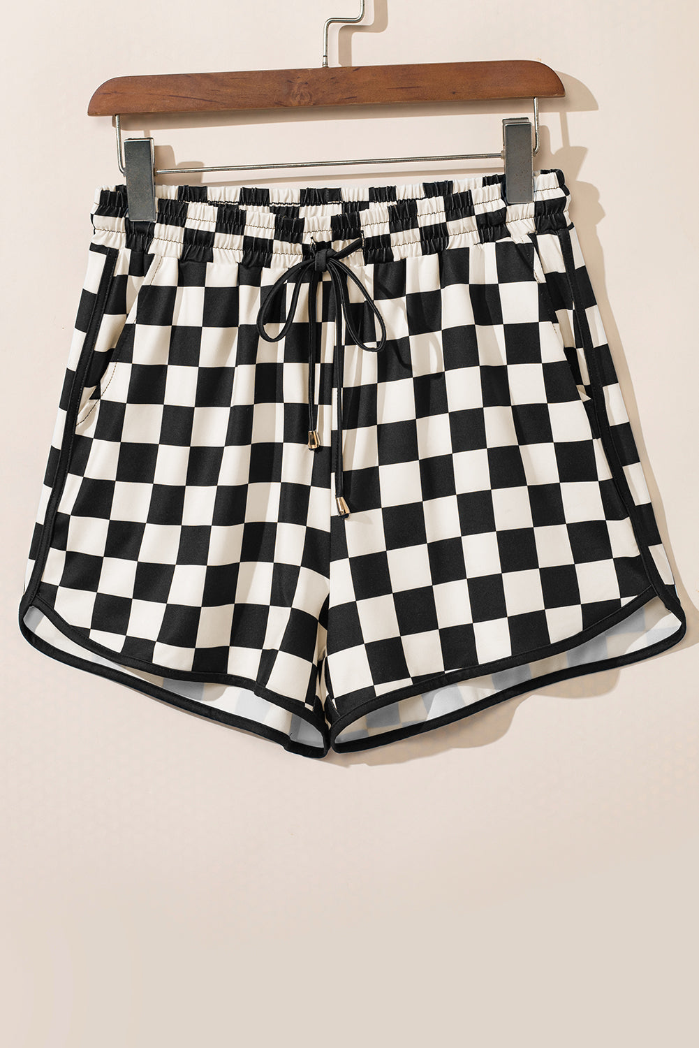 Black and white checkered shorts on a hanger against a beige background