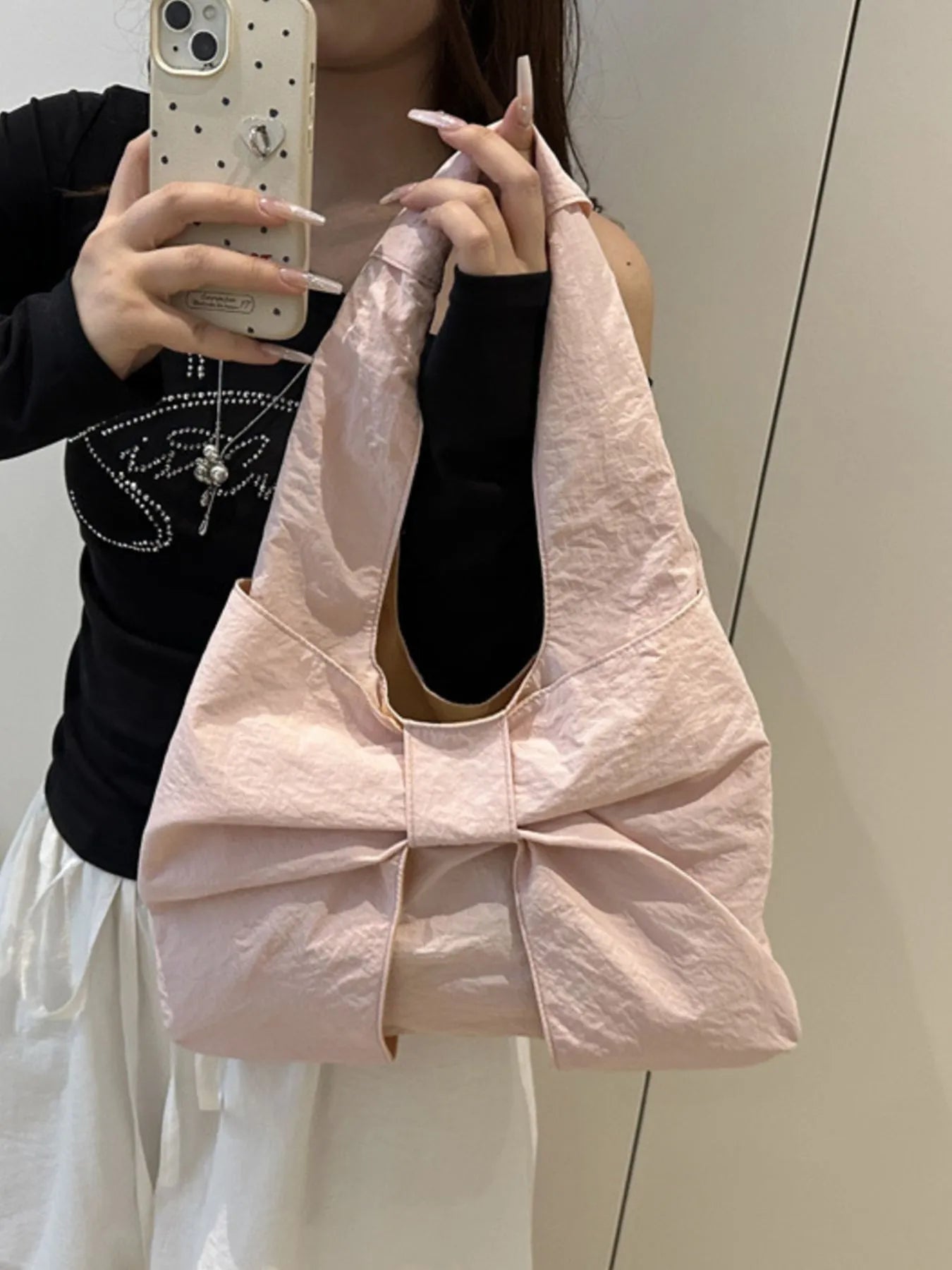 Person holding a light pink bag with a bow detail, wearing a black top and white pants.