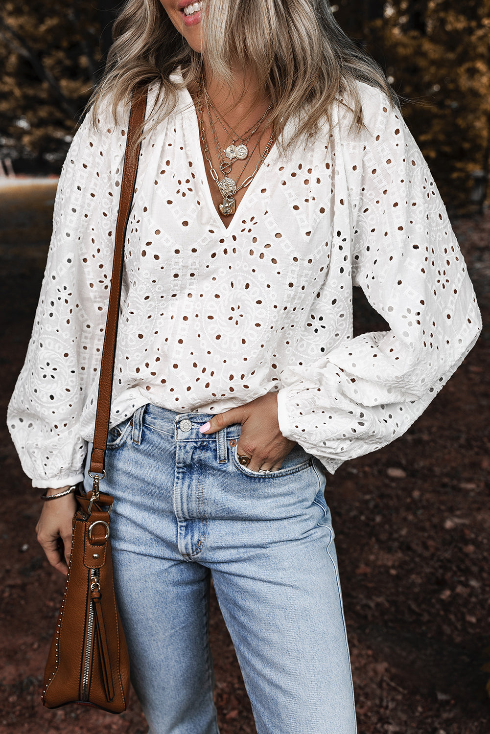 Woman wearing a white blouse with black polka dots and blue jeans, holding a brown leather bag.