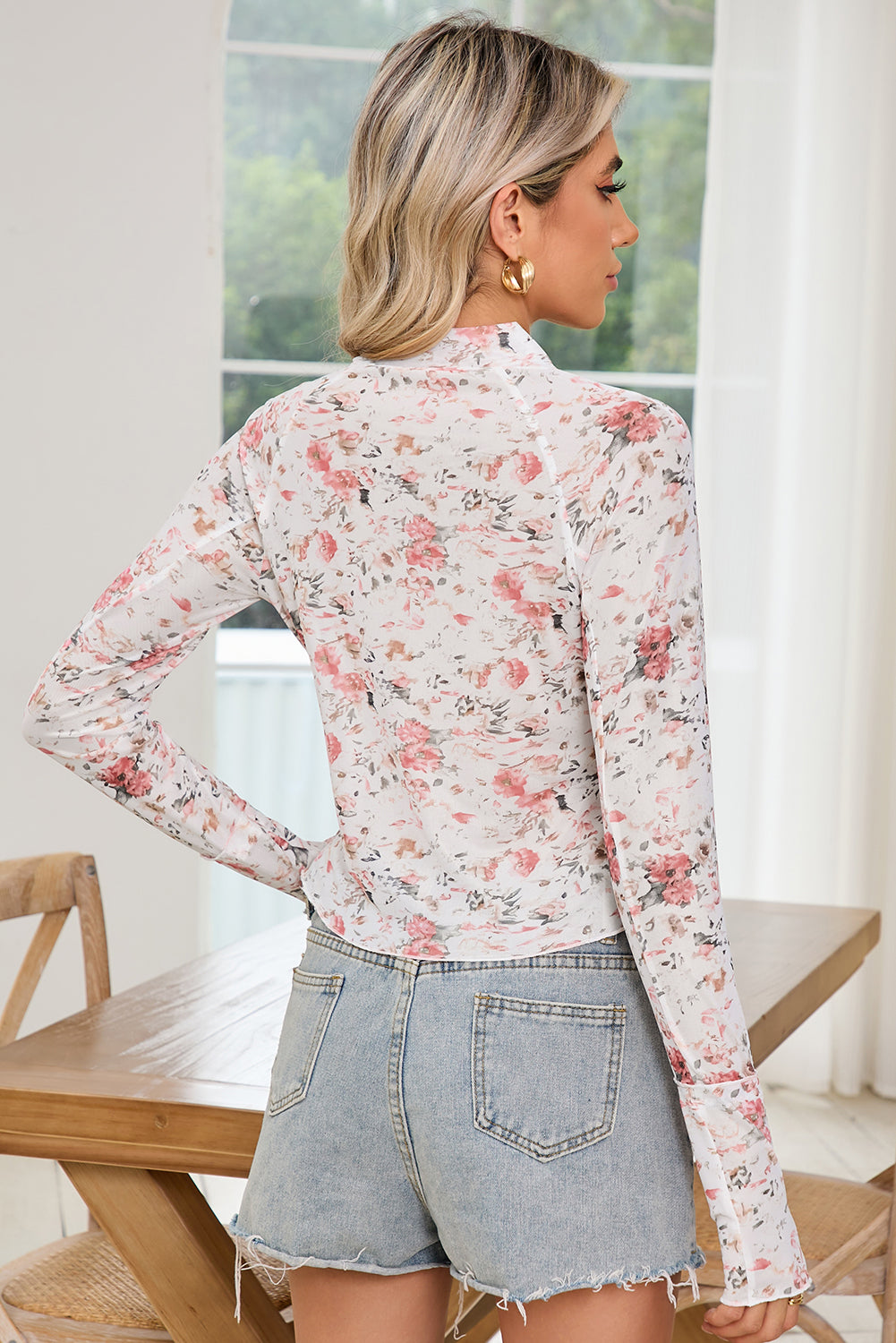 Woman wearing a floral blouse and denim shorts in a bright room.