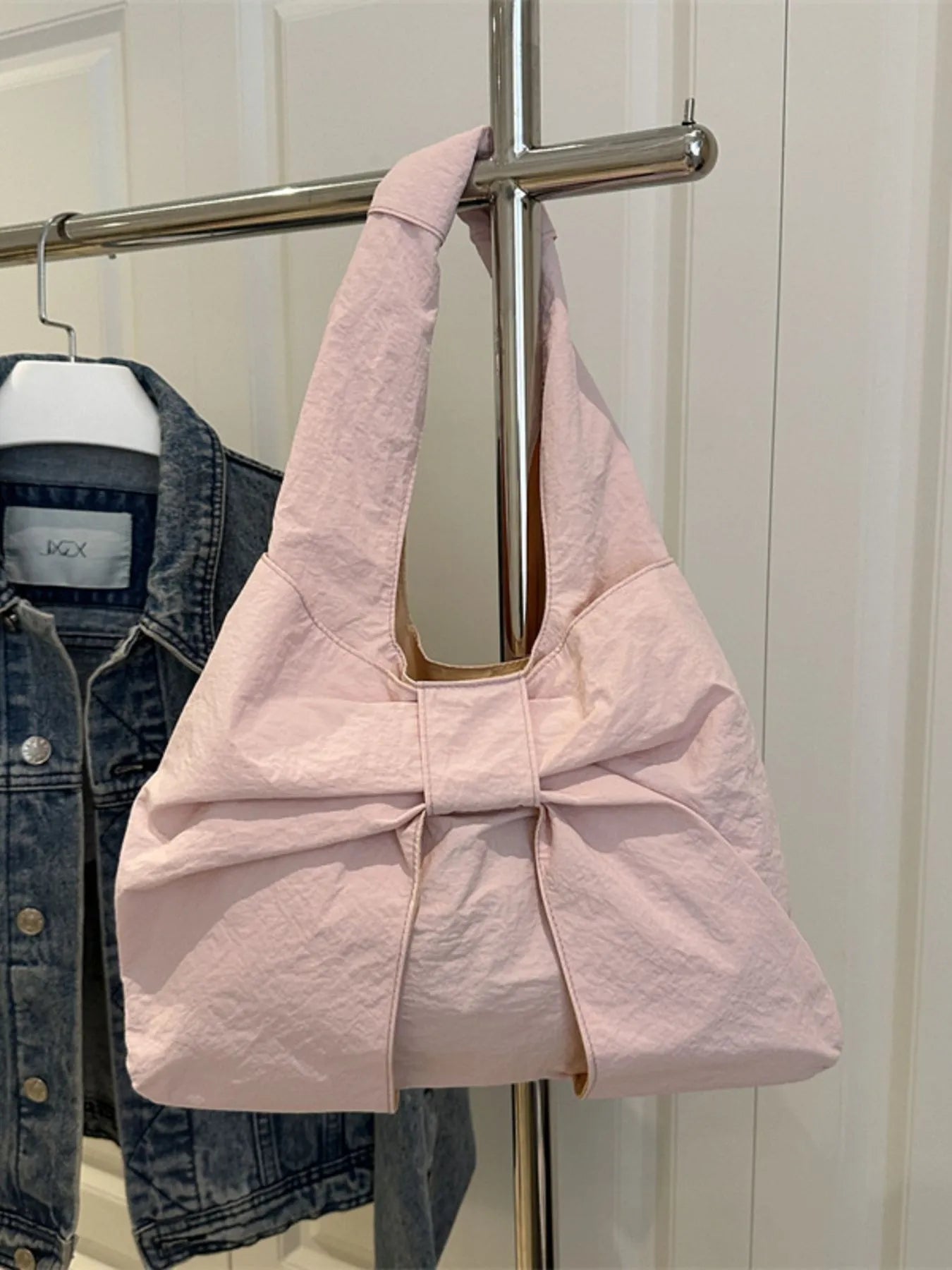 Pink bag with a bow detail hanging on a rack next to denim jeans.