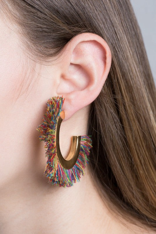 Multicolored fringe earring worn by a person with a neutral background
