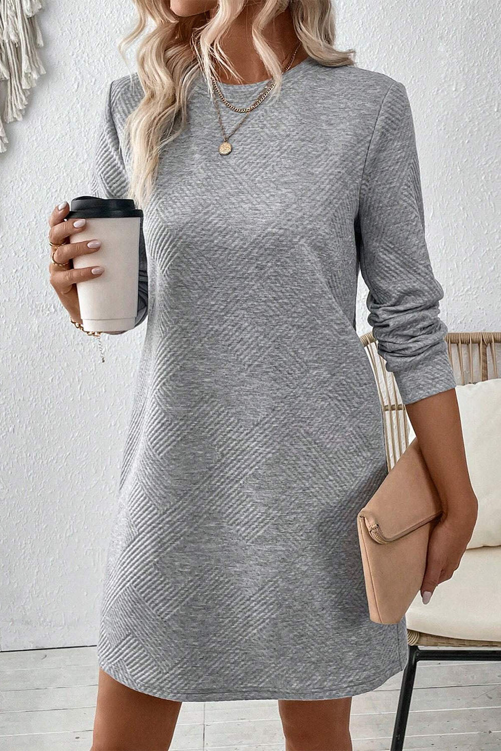 Woman wearing a gray long-sleeve dress holding a coffee cup indoors.